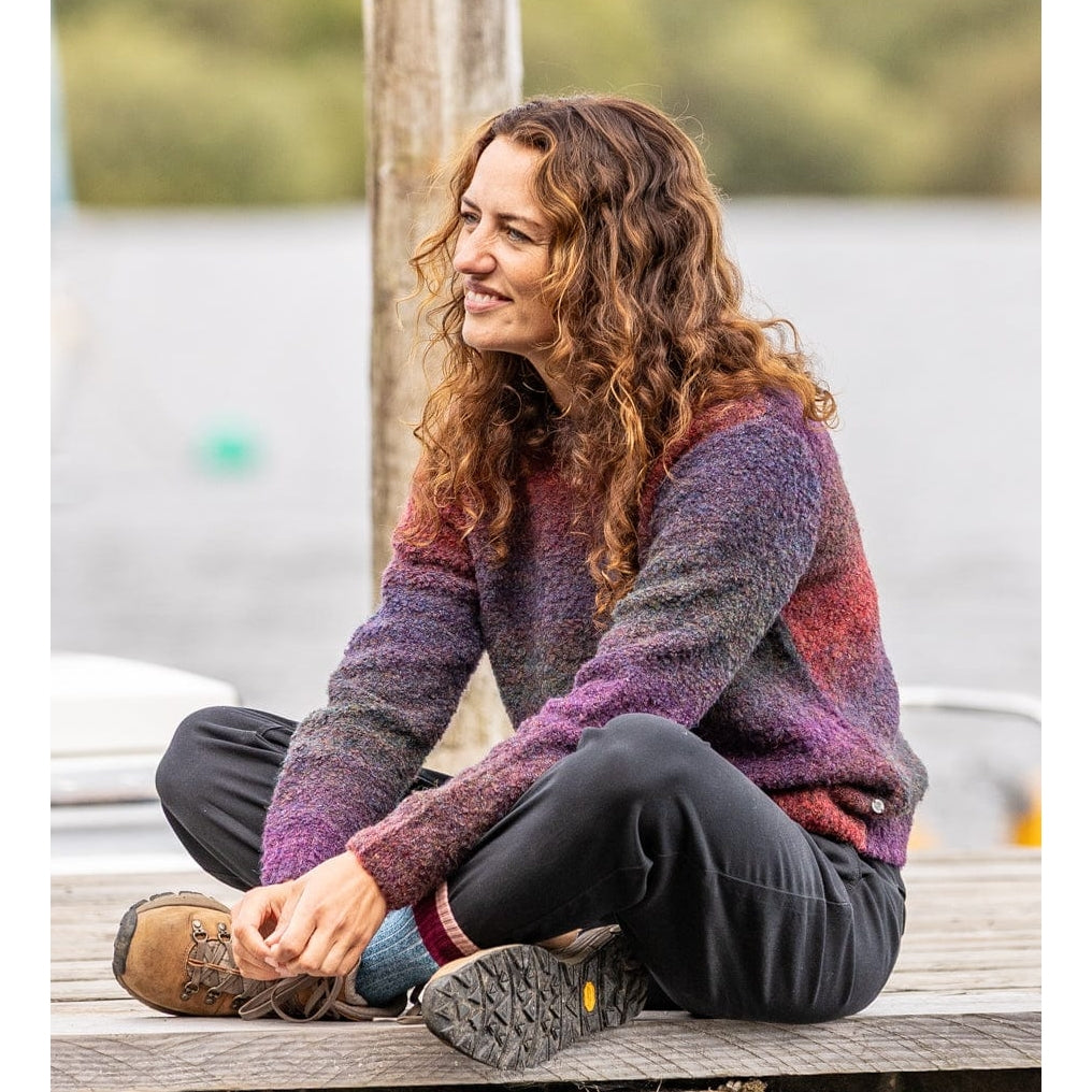 Woman sitting on a wooden dock wearing a Saltrock purple and red knitted Bowden jumper.