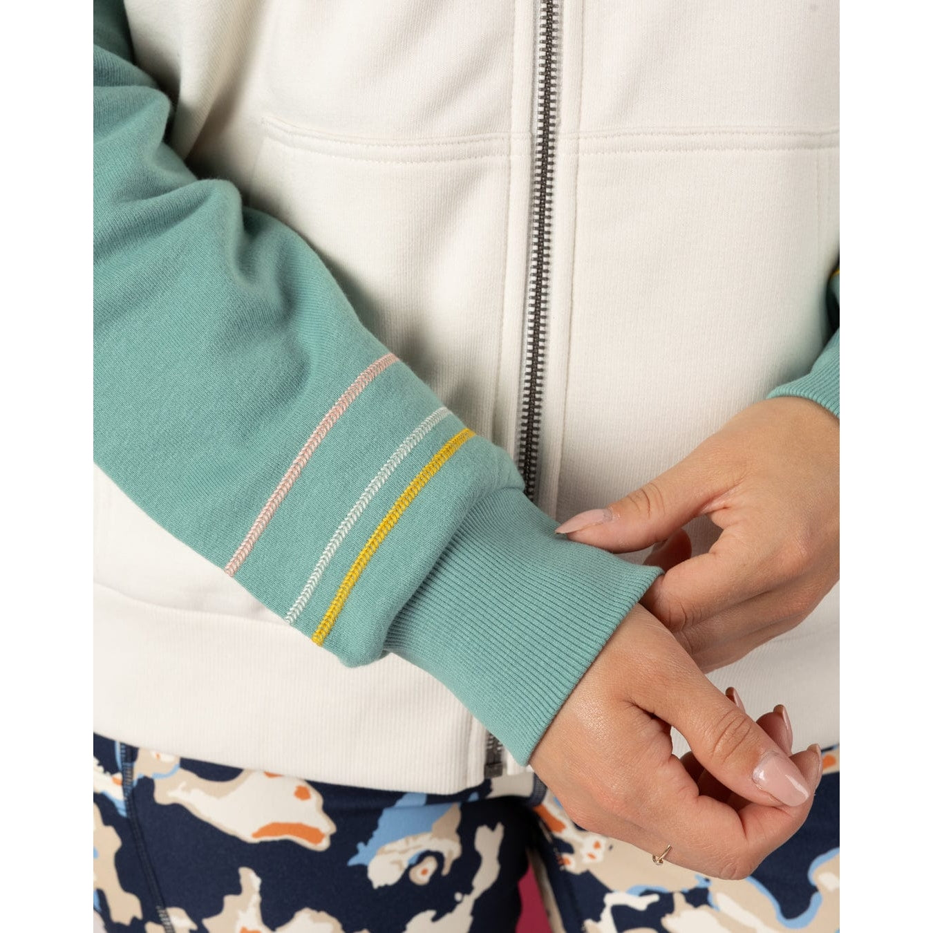 Close-up of a woman wearing a Saltrock Links Contrast light blue and cream zip hoodie with embroidered line sleeve detail