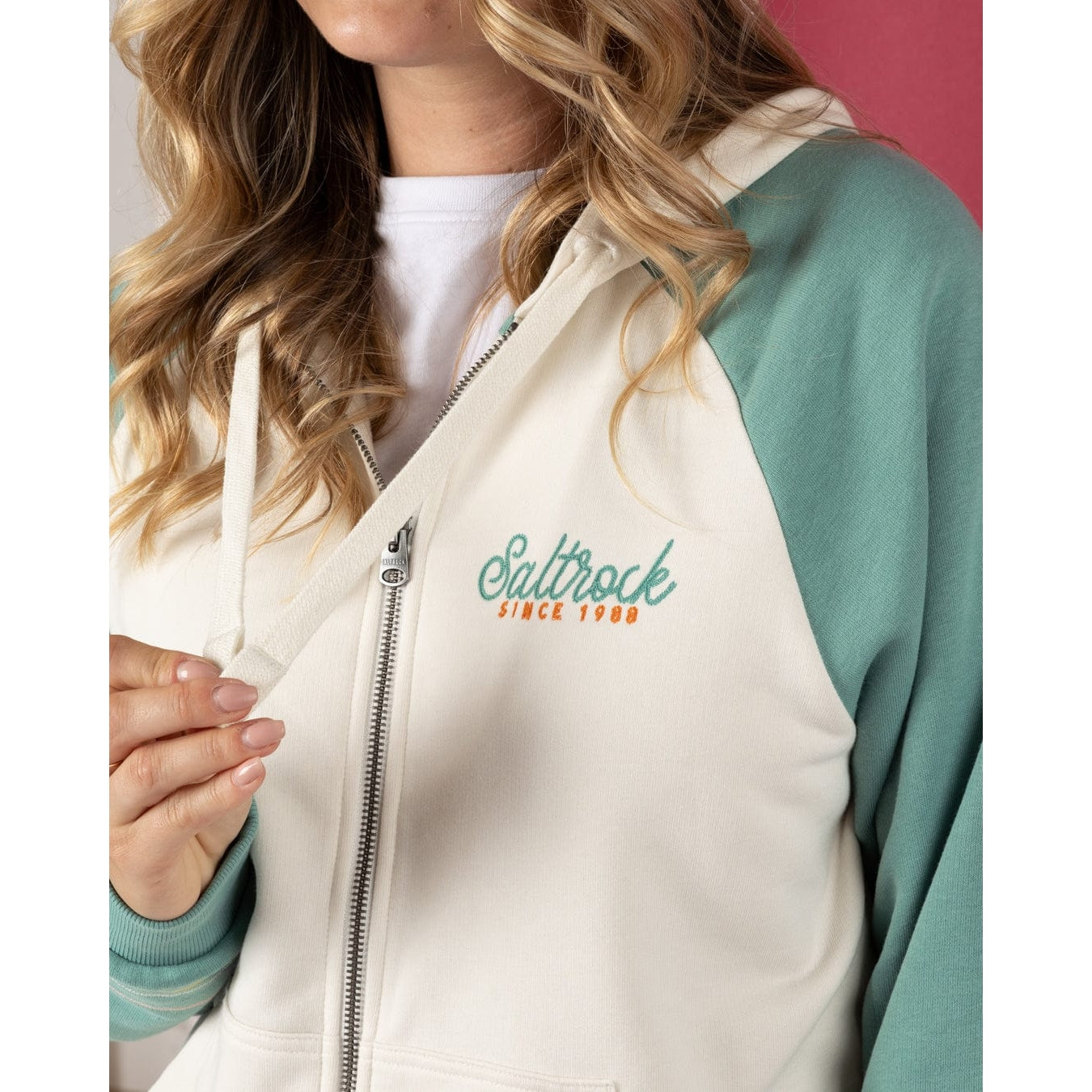Close up of a womens Saltrock Links Contrast zip hoodie in cream with light blue raglan sleeves and logo on the chest