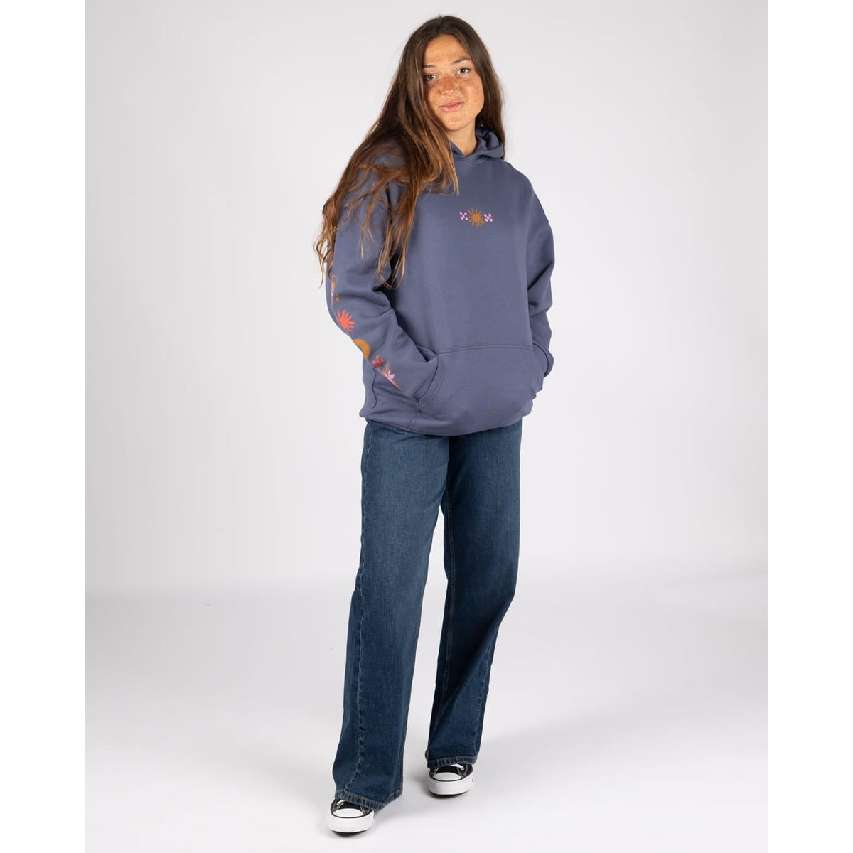A woman wearing a Saltrock Athena longline pop hoodie in dark blue with a small print on the front and along one sleeve, with blue jeans and trainers.