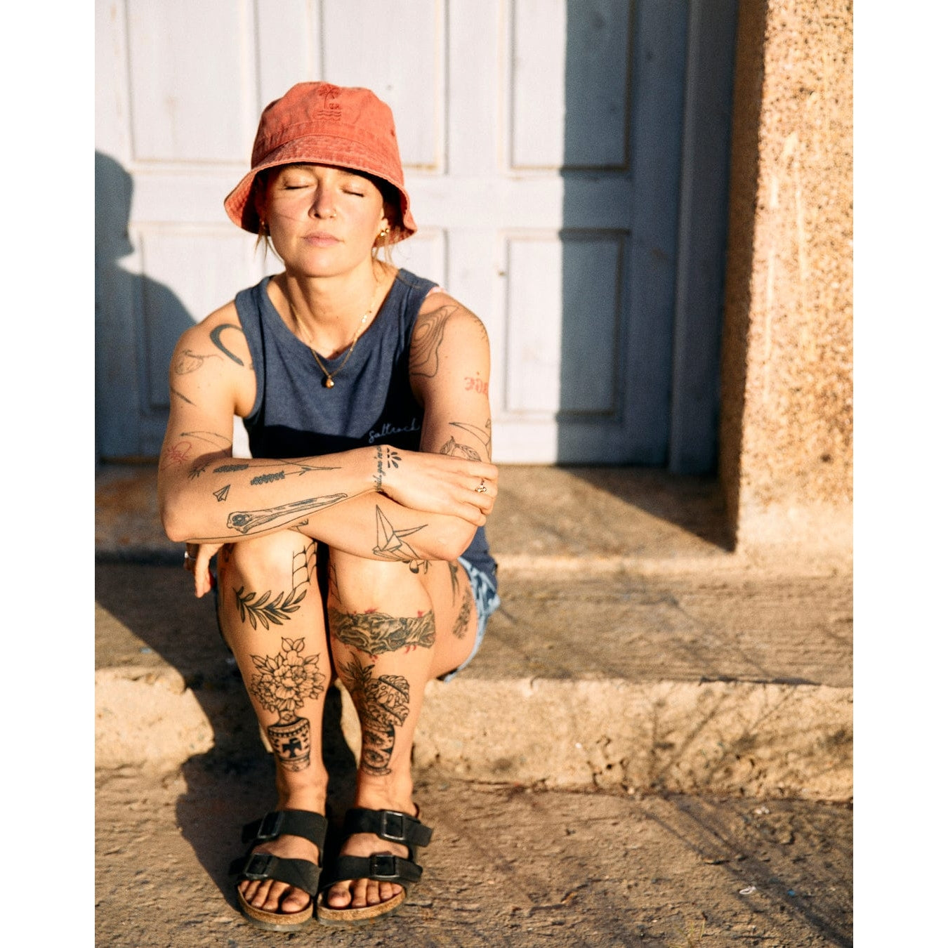 A woman wearing a blue marl Saltrock Velator essential vest sat outside on a step in the sunlight