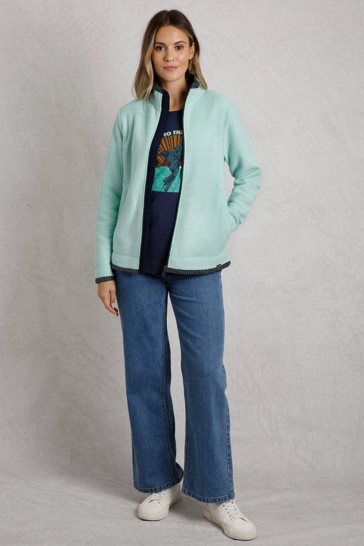 Woman wearing a light blue Weird Fish Ariana fleece jacket layered over a graphic tee and jeans