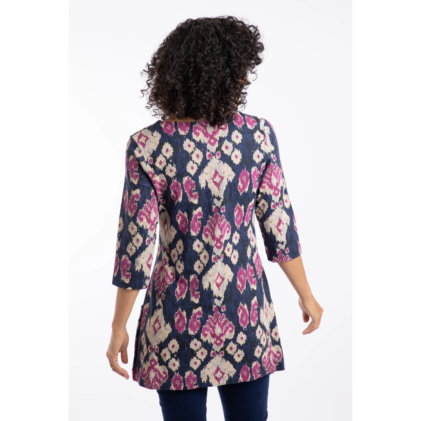 Back view of a woman wearing a Weird Fish three quarter sleeve Arielle tunic in blue with a pink-purple abstract pattern on a white background