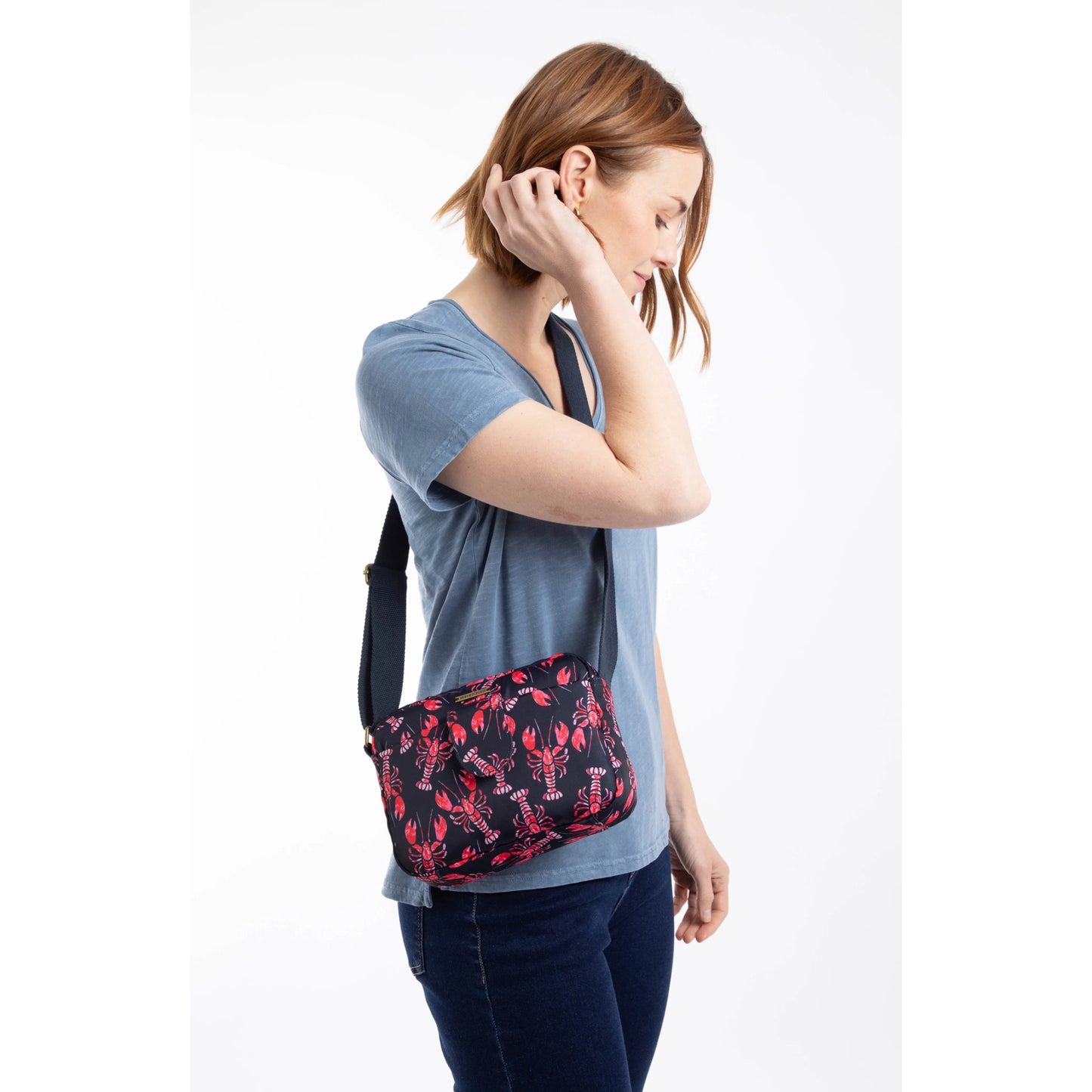 Woman wearing a Weird Fish Corrie small cross body bag, in Mid Navy with a red lobster pattern and adjustable shoulder strap.