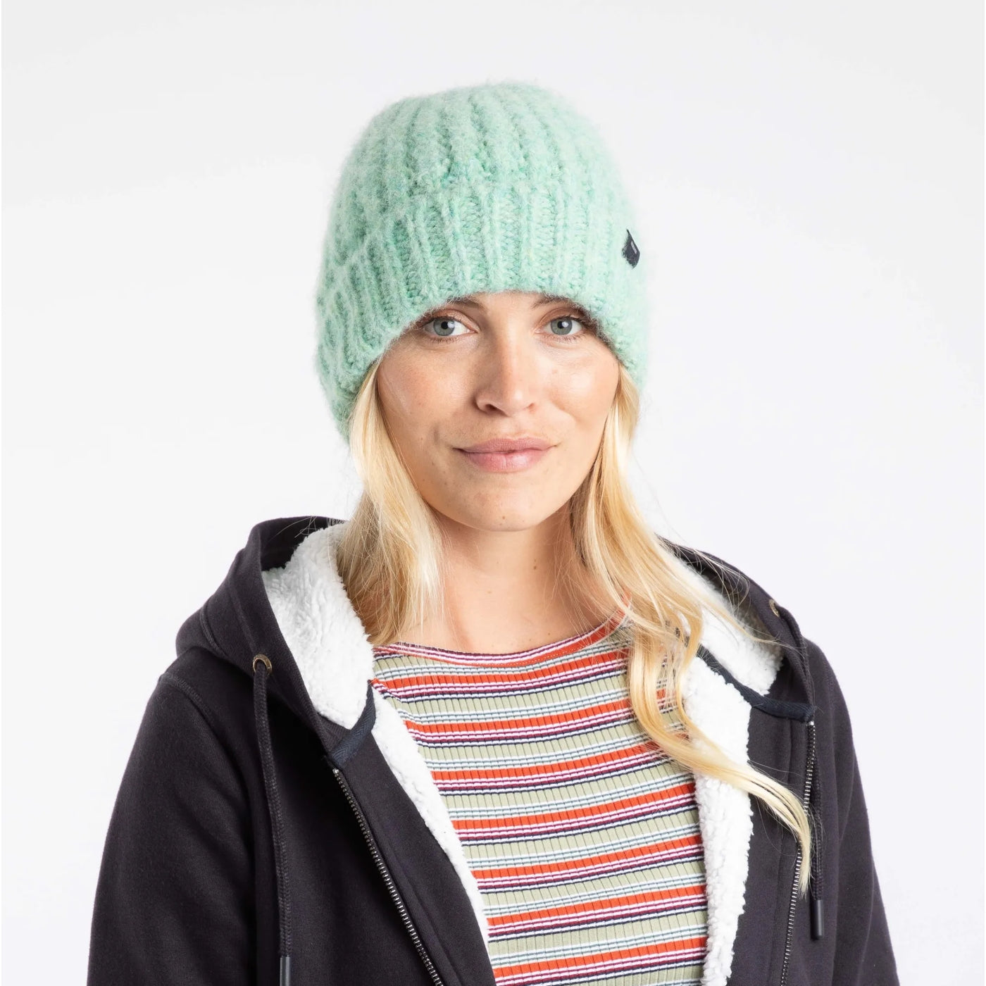 Woman wearing a Weird Fish light green Clare knitted beanie and black jacket with white lining on a white background