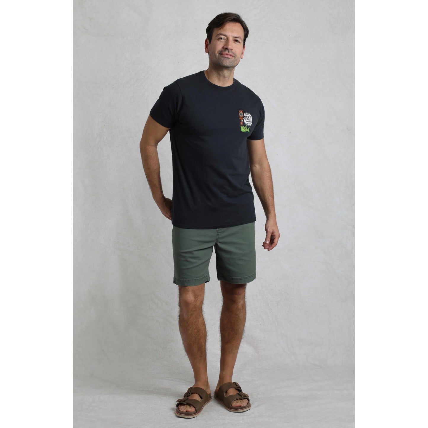Man wearing a black t-shirt with a logo and green shorts on a grey background