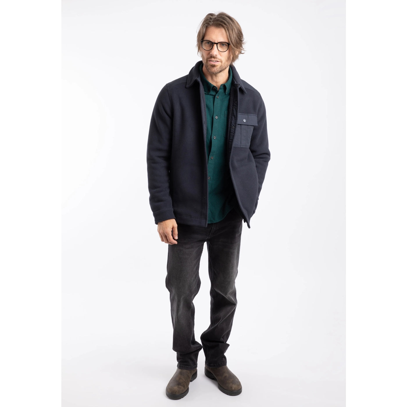 Man wearing a dark navy Weird Fish Boyd fleece jacket, green shirt, and grey pants on a white background