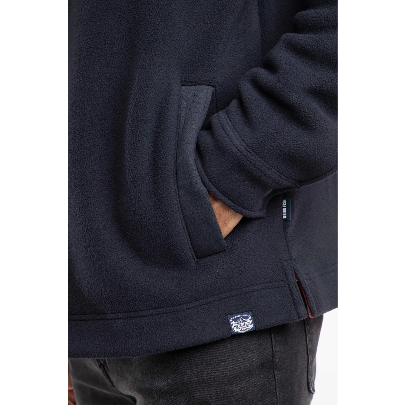 Close up of a dark navy mens Weird Fish Boyd fleece jacket pocket with a visible brand logo on a white background