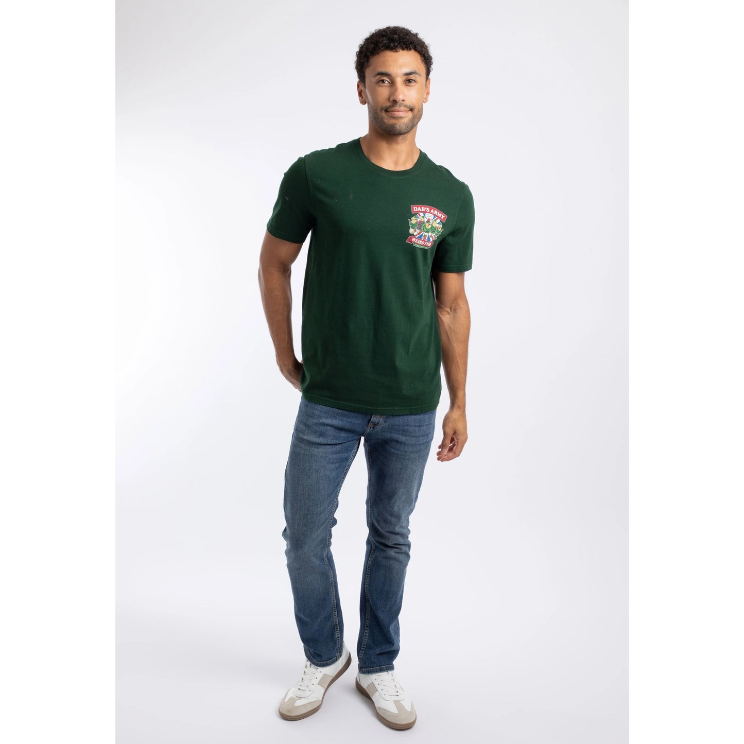 A man wearing a Weird Fish Dab's Army printed t-shirt, in beetle green, featuring a small Dad's Army TV show themed print on one side of the chest with blue jeans.