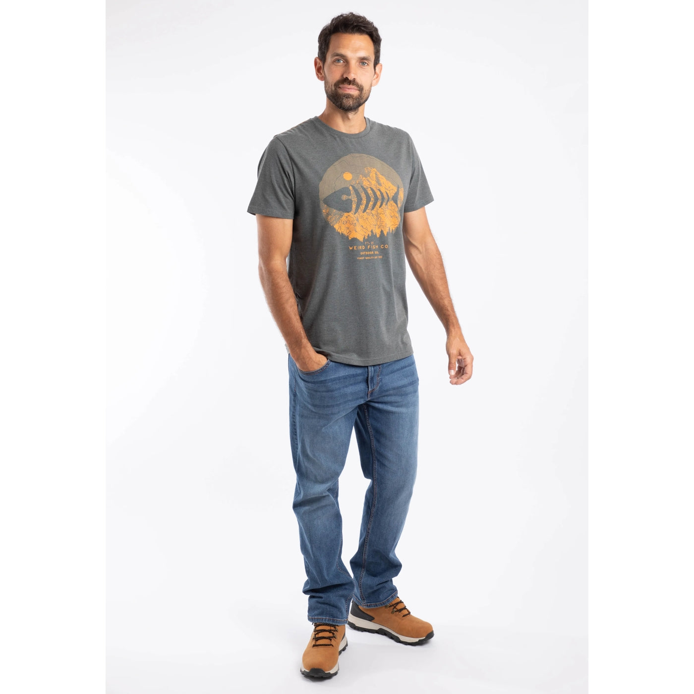Man wearing a grey Weird Fish Explorer t-shirt with an orange graphic design and blue jeans on a white background