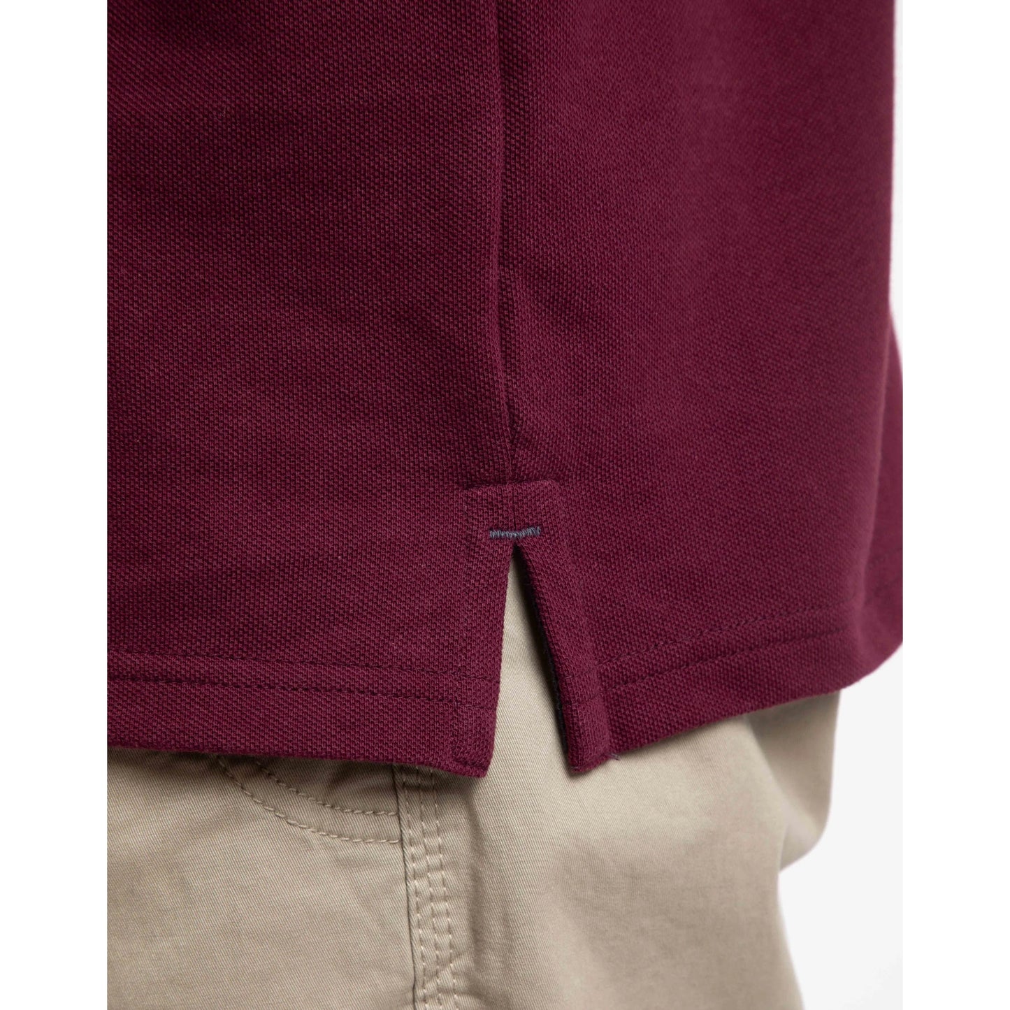 Close-up of a Weird Fish men's Miles maroon polo shirt side slit with beige pants in the background
