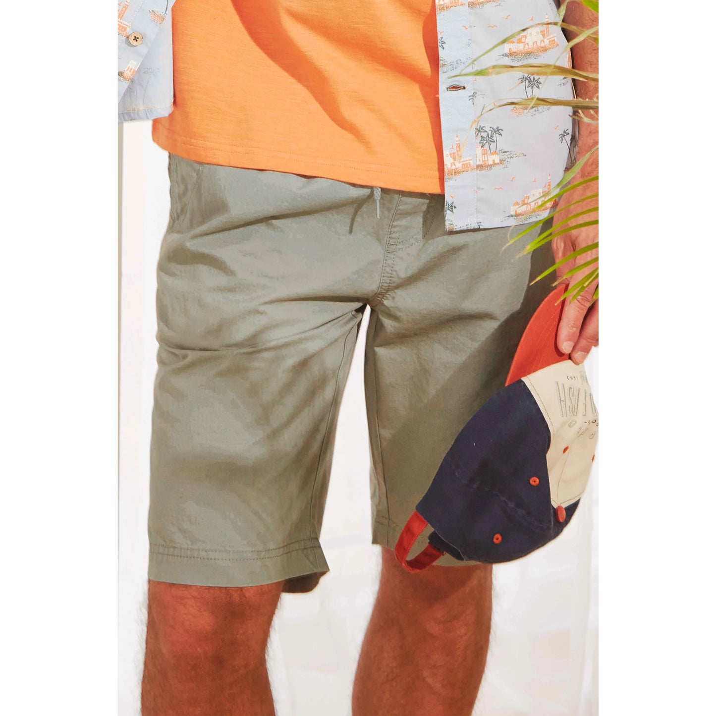 Weird Fish mens Murrisk shorts shadow in light green worn by a man holding a navy and red cap