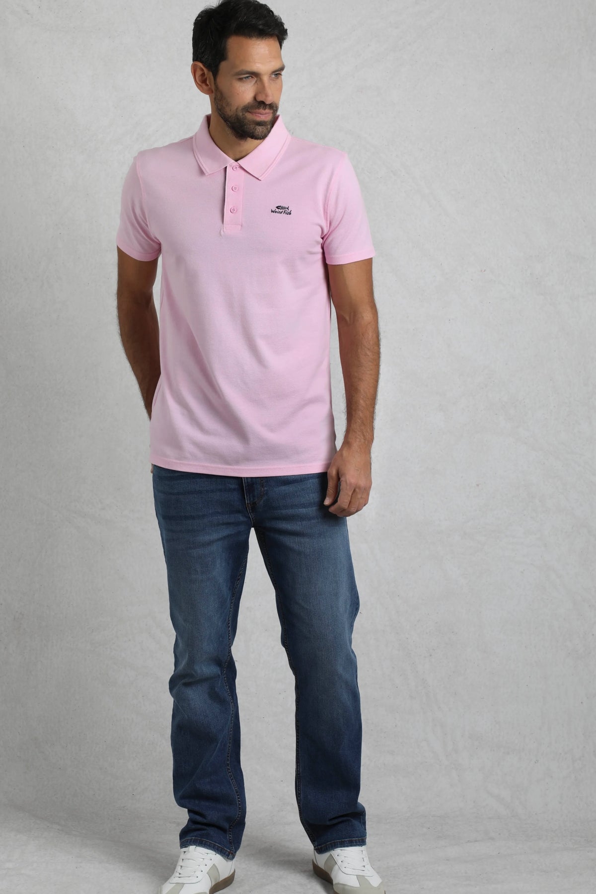 Man wearing a Weird Fish mens pink polo shirt paired with blue jeans and white sneakers