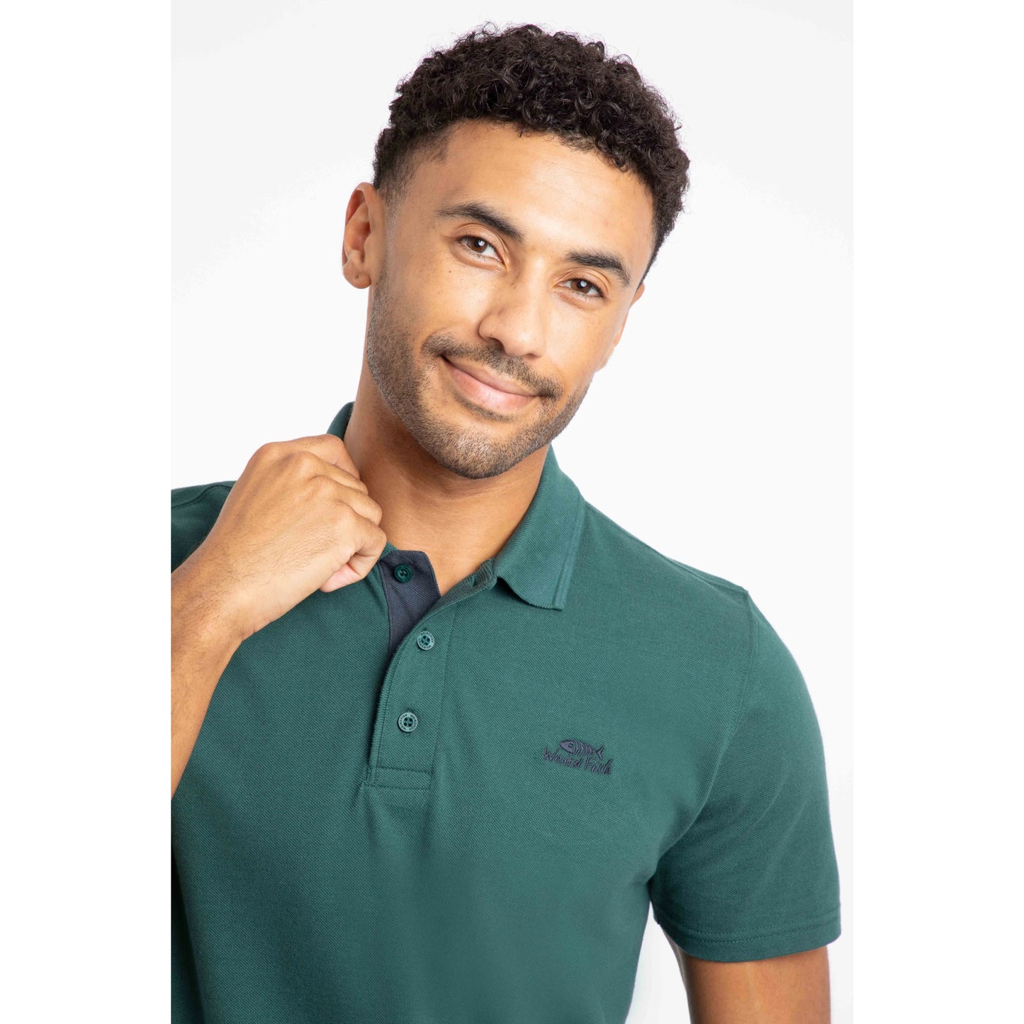 Weird Fish mens polo shirt Forest Green worn by man with short curly hair and casual pose