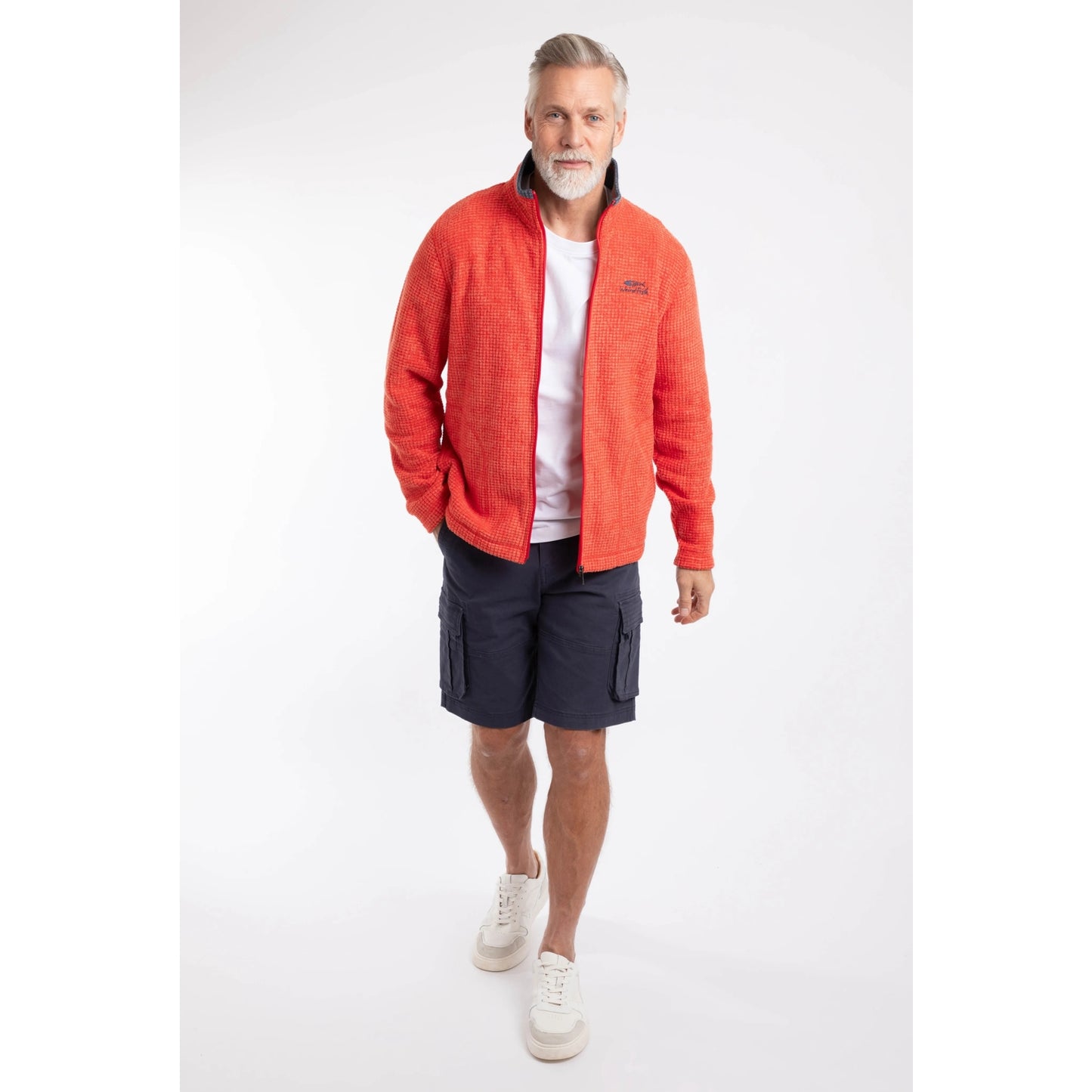 A man wearing a Weird Fish full zip Shires grid textured fleece in bright Orange Spice with a white t-shirt, navy shorts and white trainers