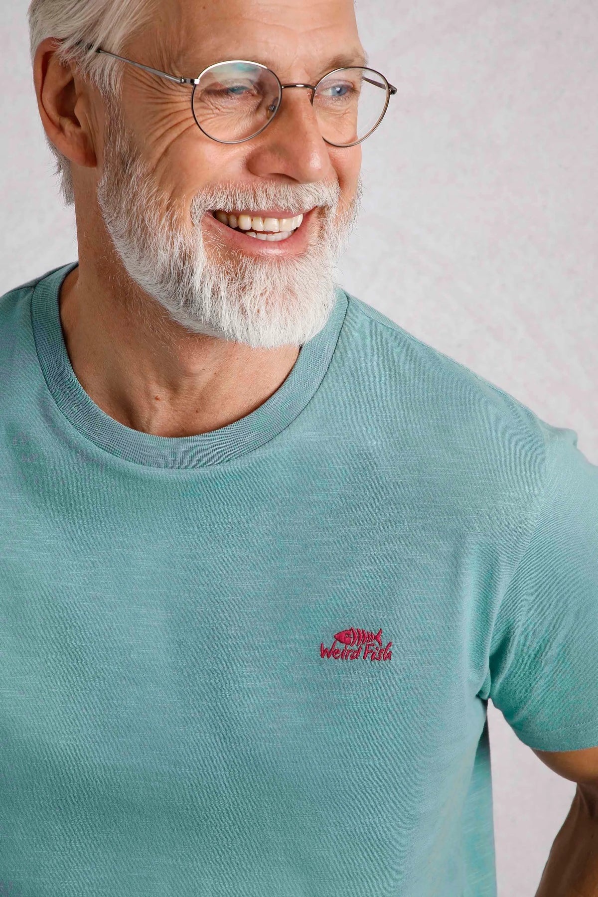 Weird Fish mens t-shirt blue with red logo worn by smiling older man with glasses and white beard