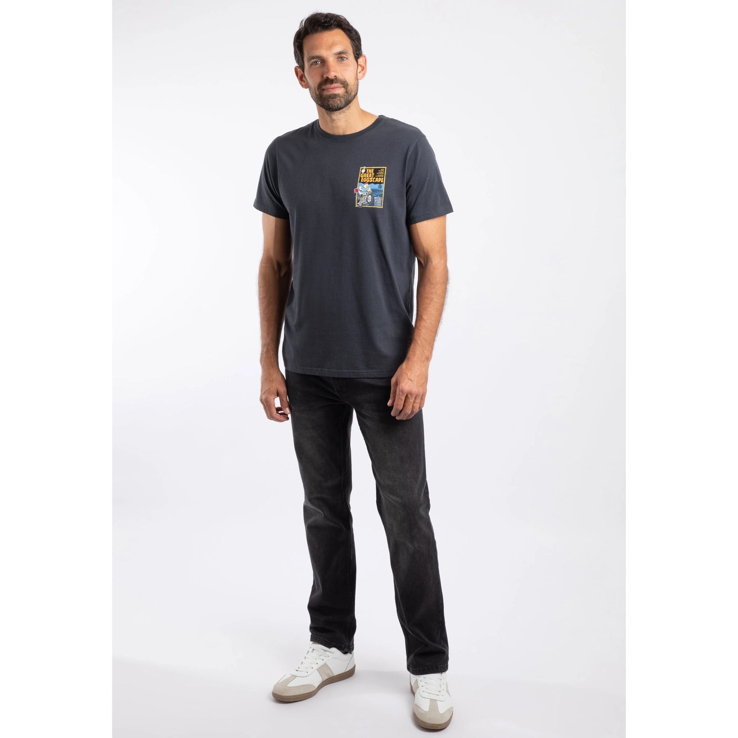 Man wearing a navy t-shirt with a print and dark jeans on a white background
