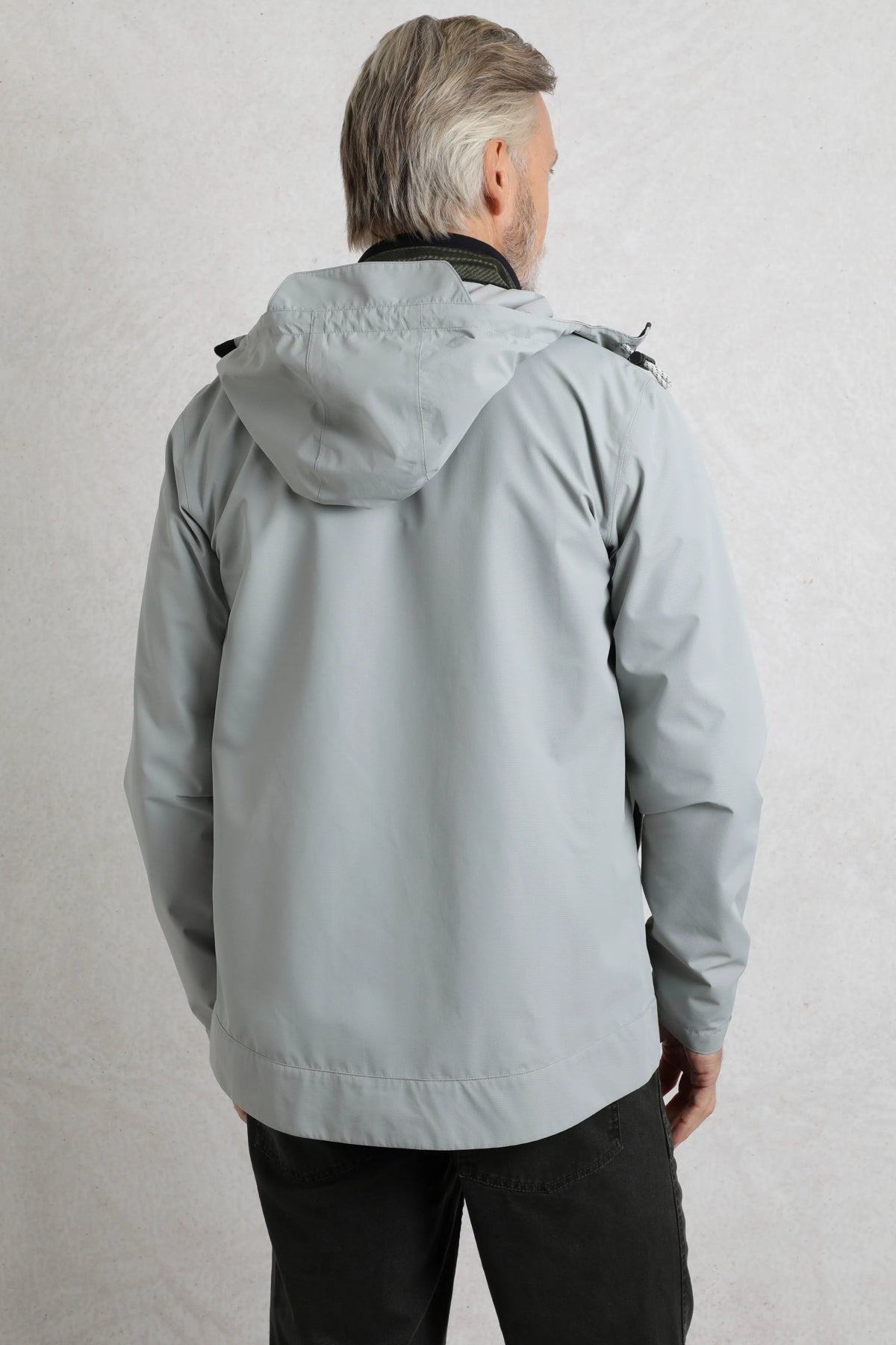 Back view of a man wearing a Weird Fish mens waterproof jacket grey with hood in a light grey color