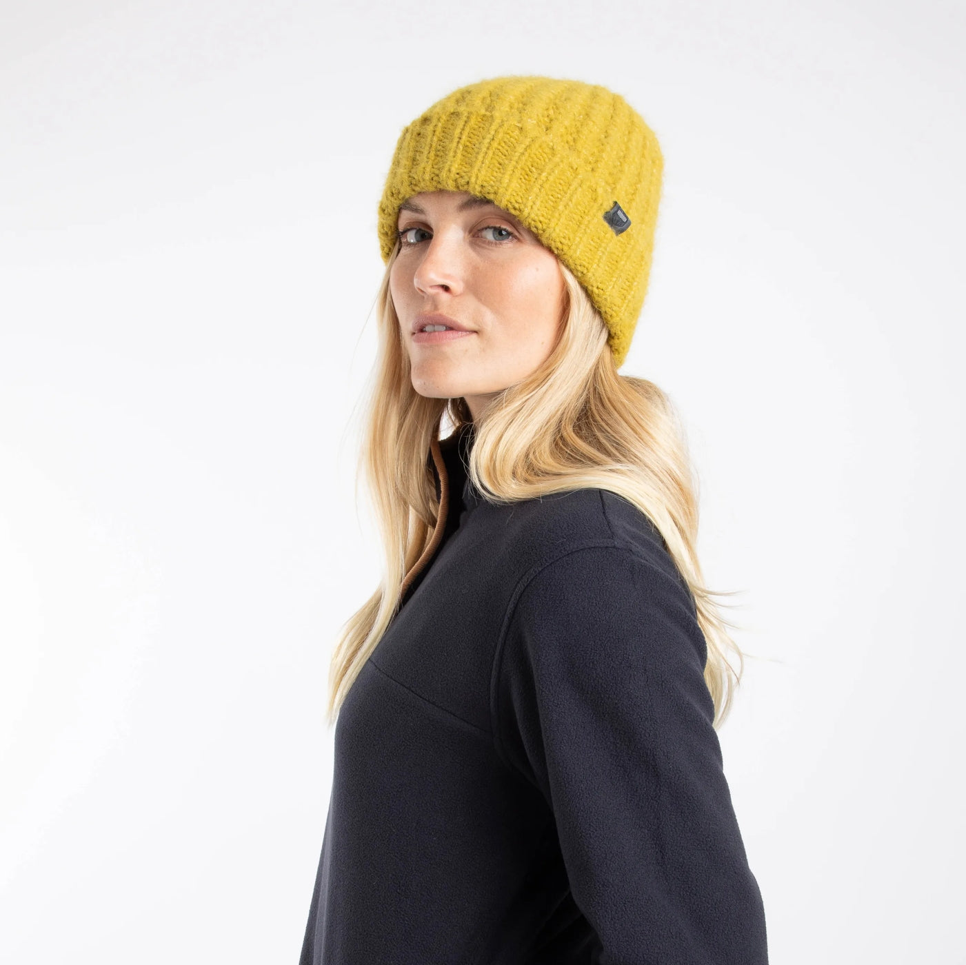 Woman wearing a Weird Fish Clare knitted beanie in Antique Moss yellow on a white background