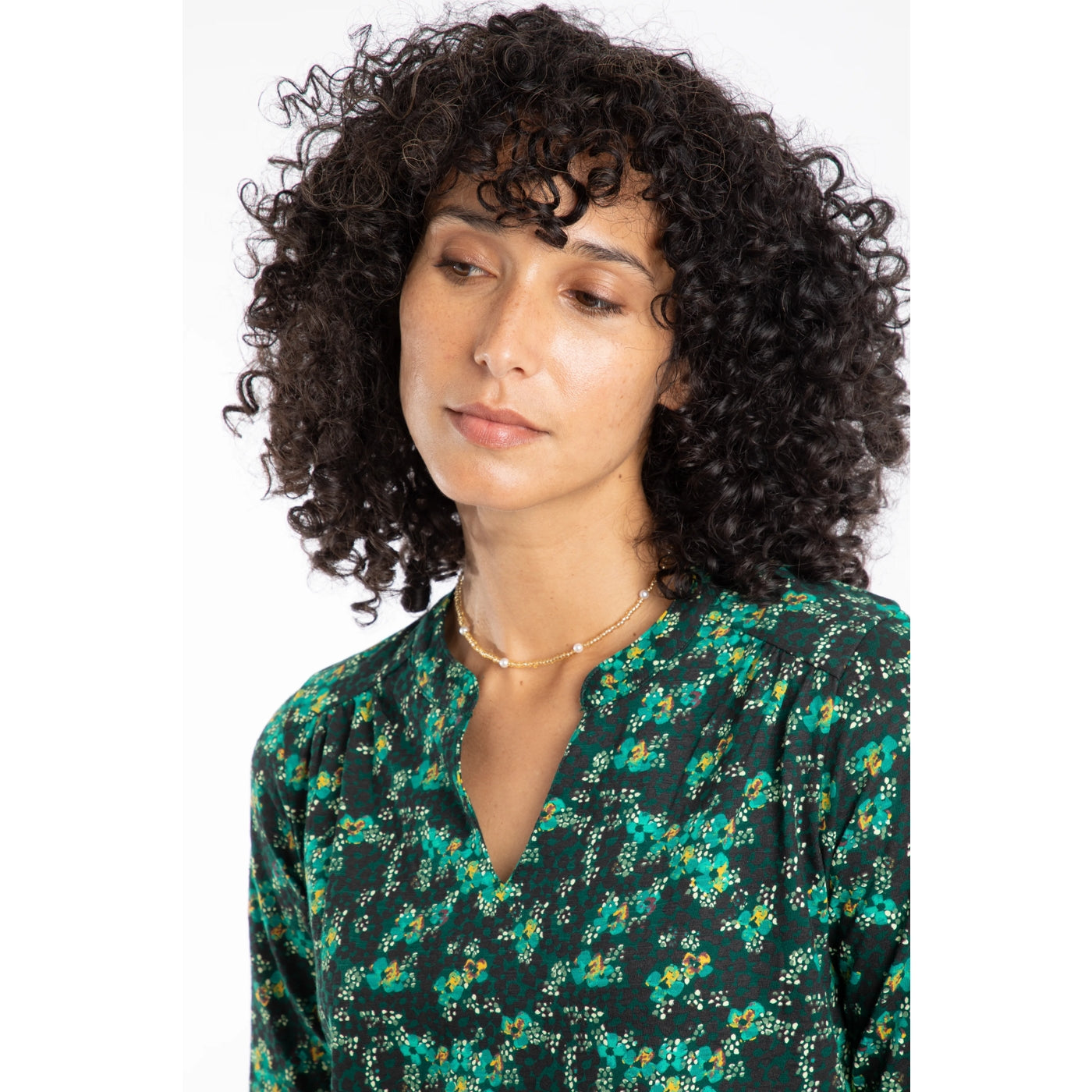 Woman with curly hair wearing a Weird Fish long sleeve green floral patterned Brooke t-shirt on a white background