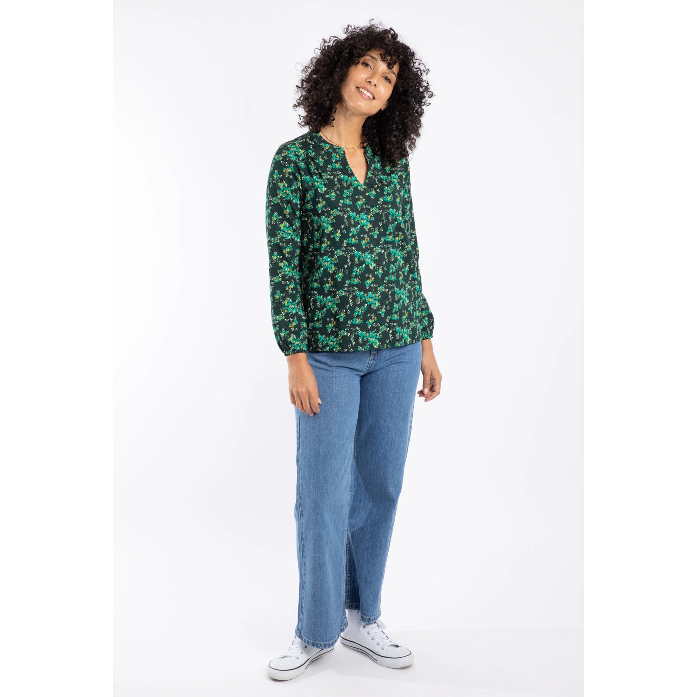Woman wearing a Weird Fish long sleeve green floral Brooke Top and blue jeans on a white background