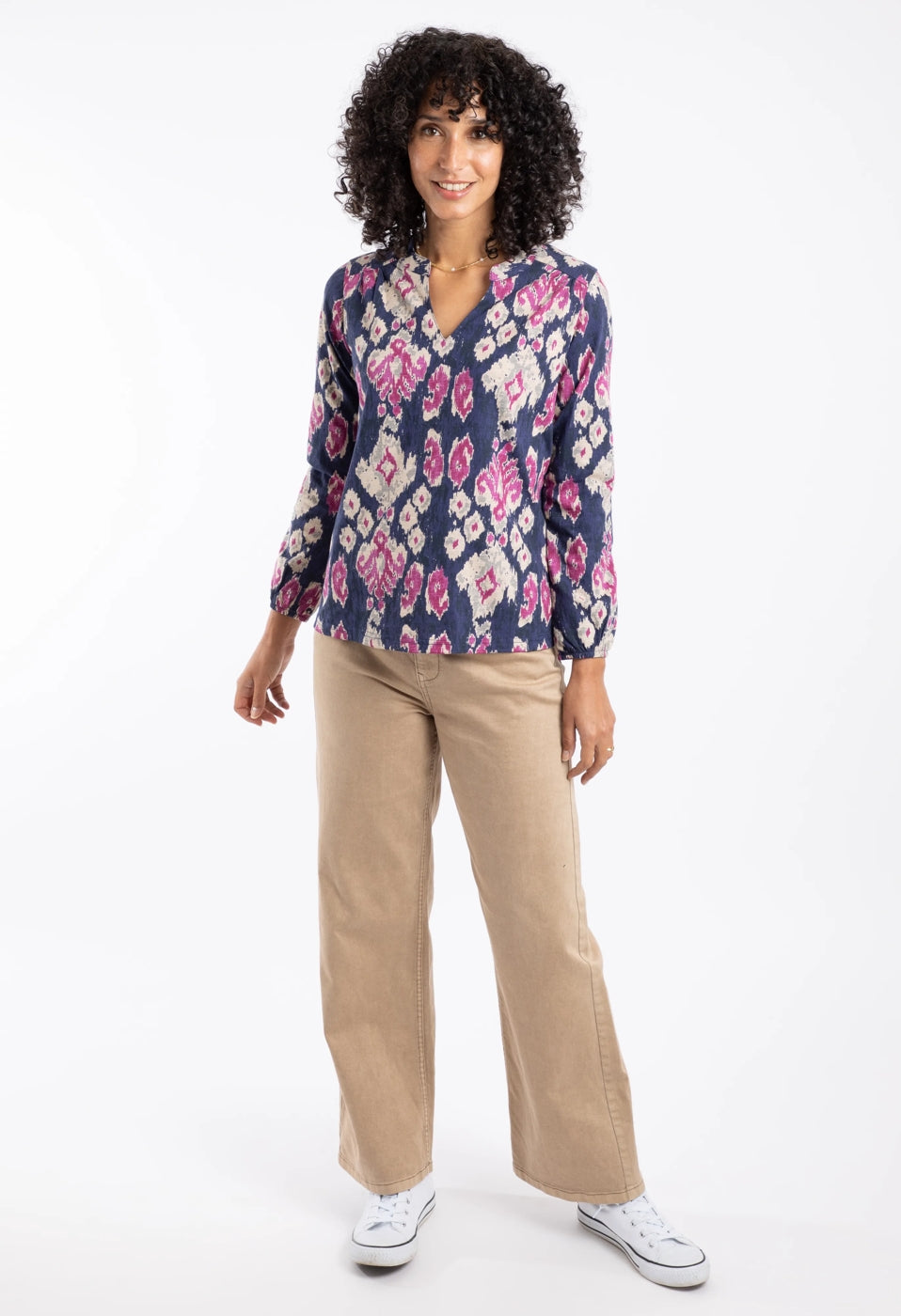 Woman wearing a Weird Fish abstract patterned Brooke top in blue and pink with beige pants on a white background
