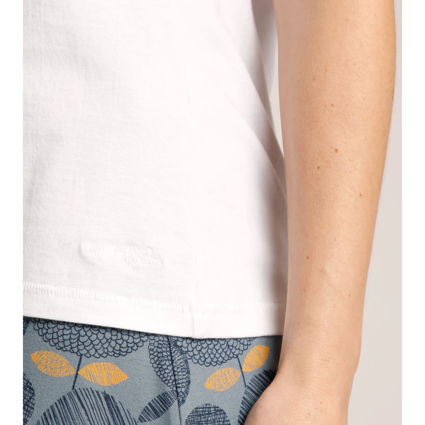 Close-up of Weird Fish womens Calle plain white vest hem and side with patterned blue and yellow pants