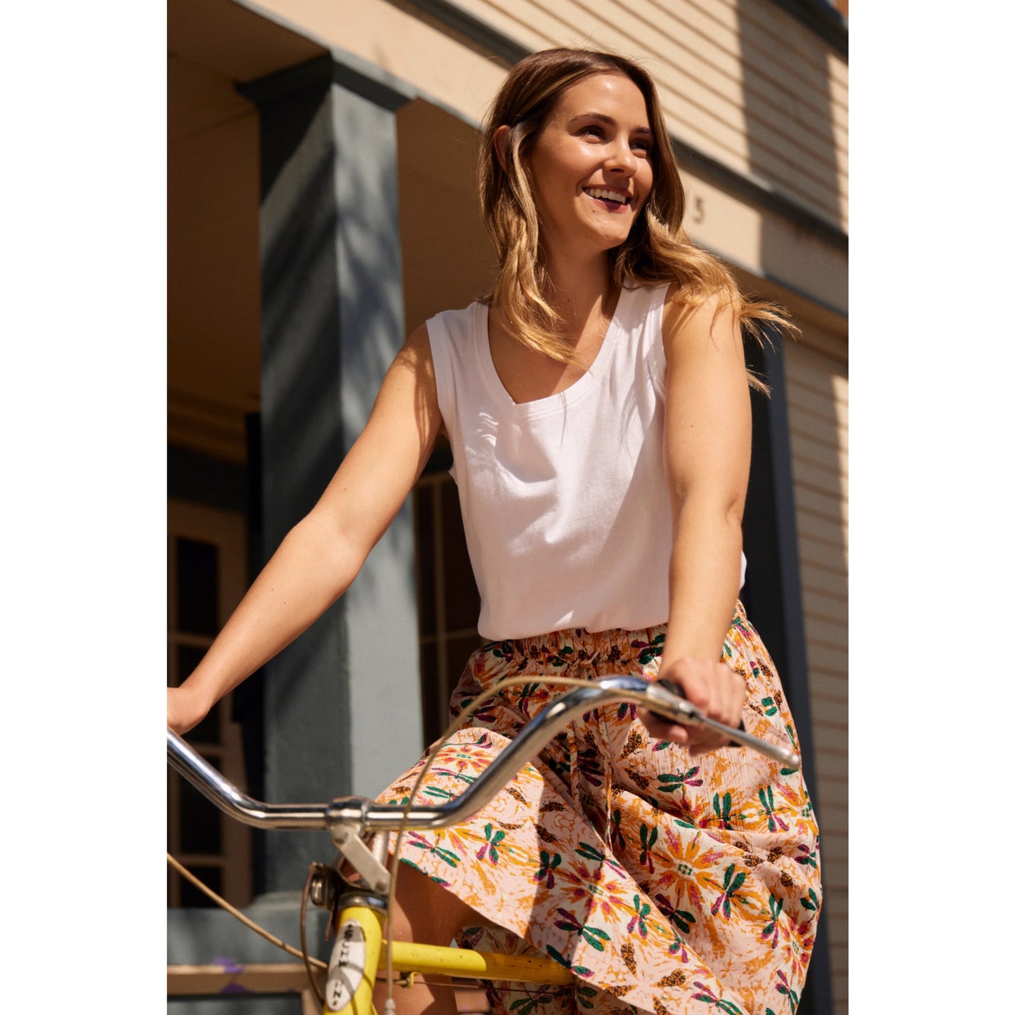 Woman wearing Weird Fish womens plain white Calle vest and floral skirt riding a yellow bicycle outdoors