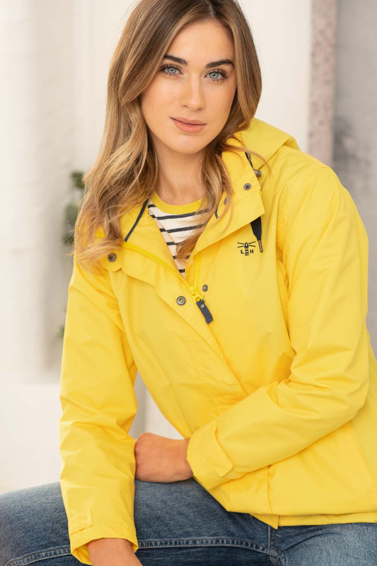 Lighthouse womens jacket yellow worn by a woman with blue jeans and striped shirt indoors
