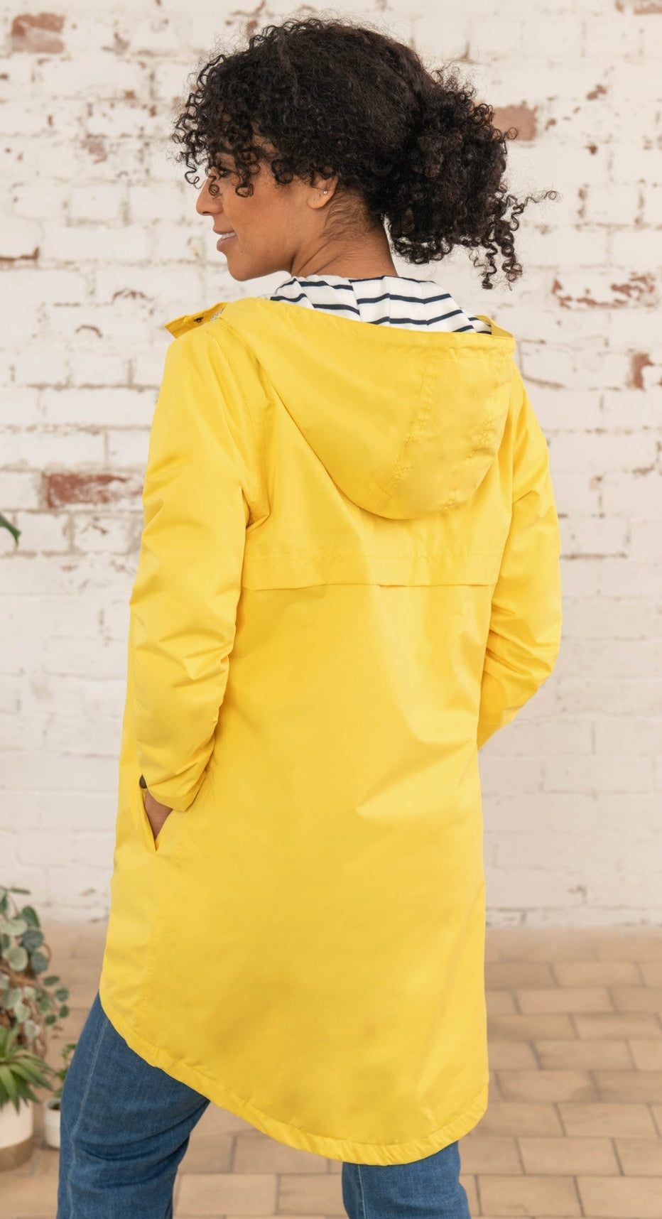 Lighthouse yellow waterproof jacket womens modeled from back with hood up and hands in pockets