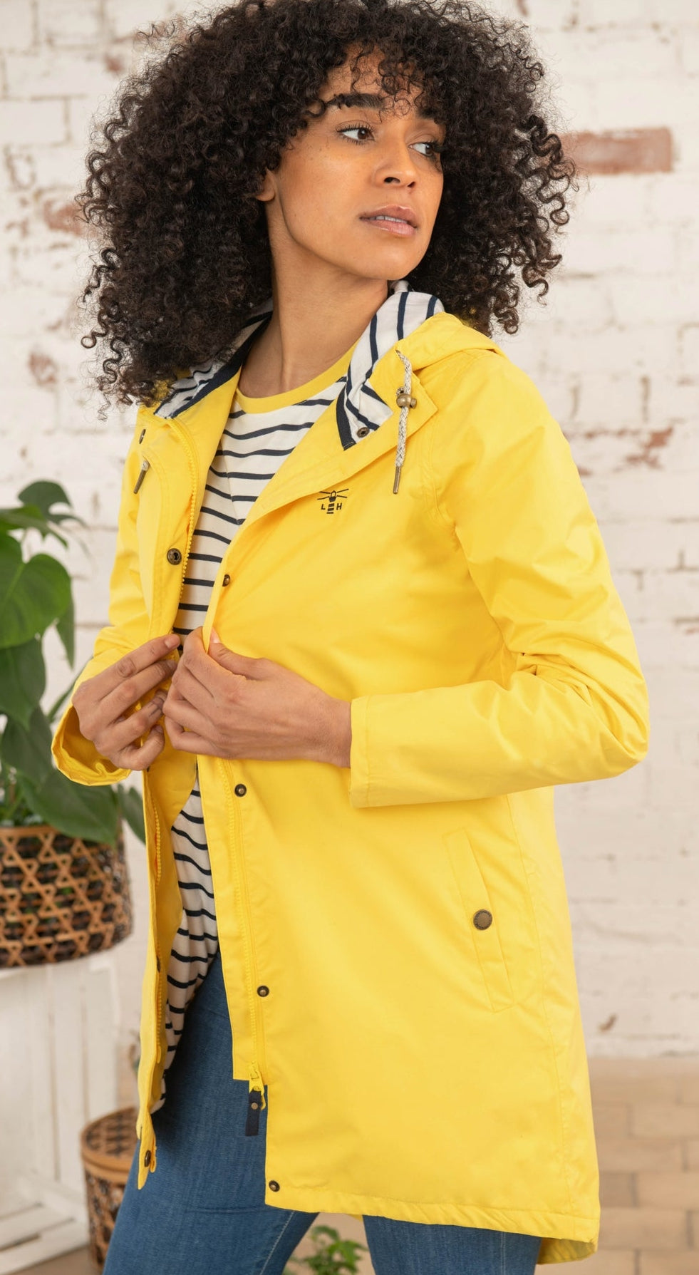 Lighthouse yellow waterproof jacket womens worn by model with curly hair over striped shirt and jeans
