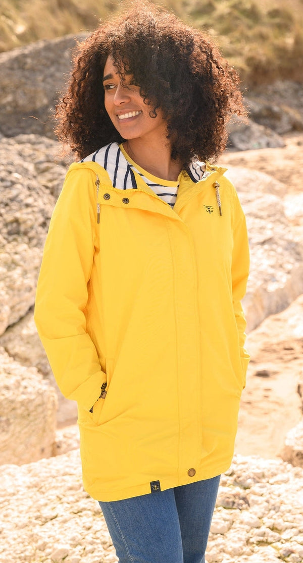 Lighthouse yellow waterproof jacket womens worn by smiling model outdoors on rocky background