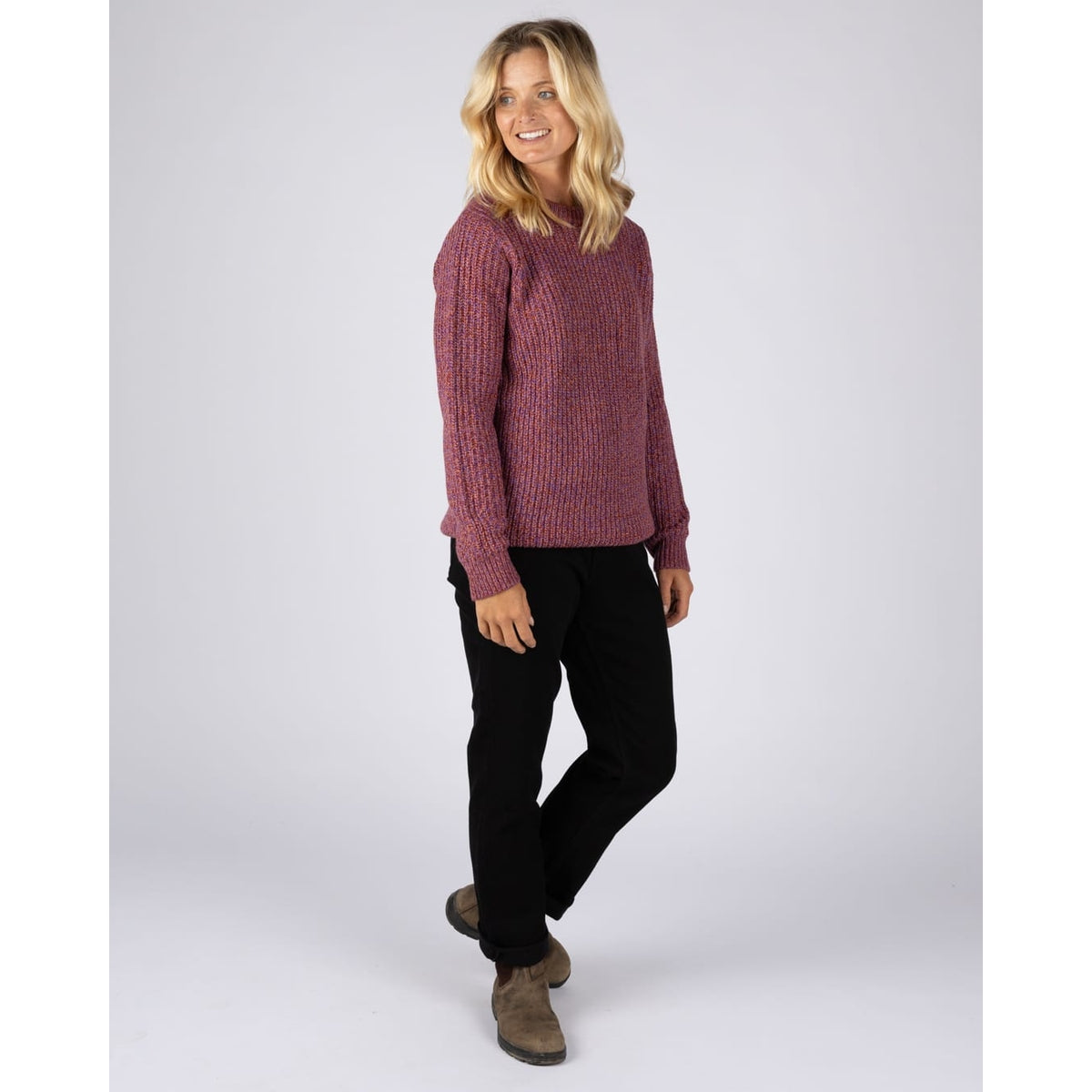 A woman wearing a Saltrock Lucy crew neck longline knitted jumper in purple with black trousers and boots.