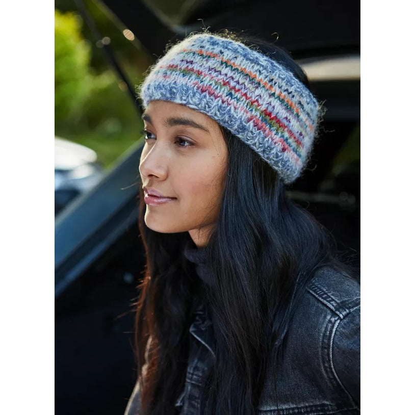 Main view of a woman wearing a colourful knitted Pachamama Coroico headband with a blurred background
