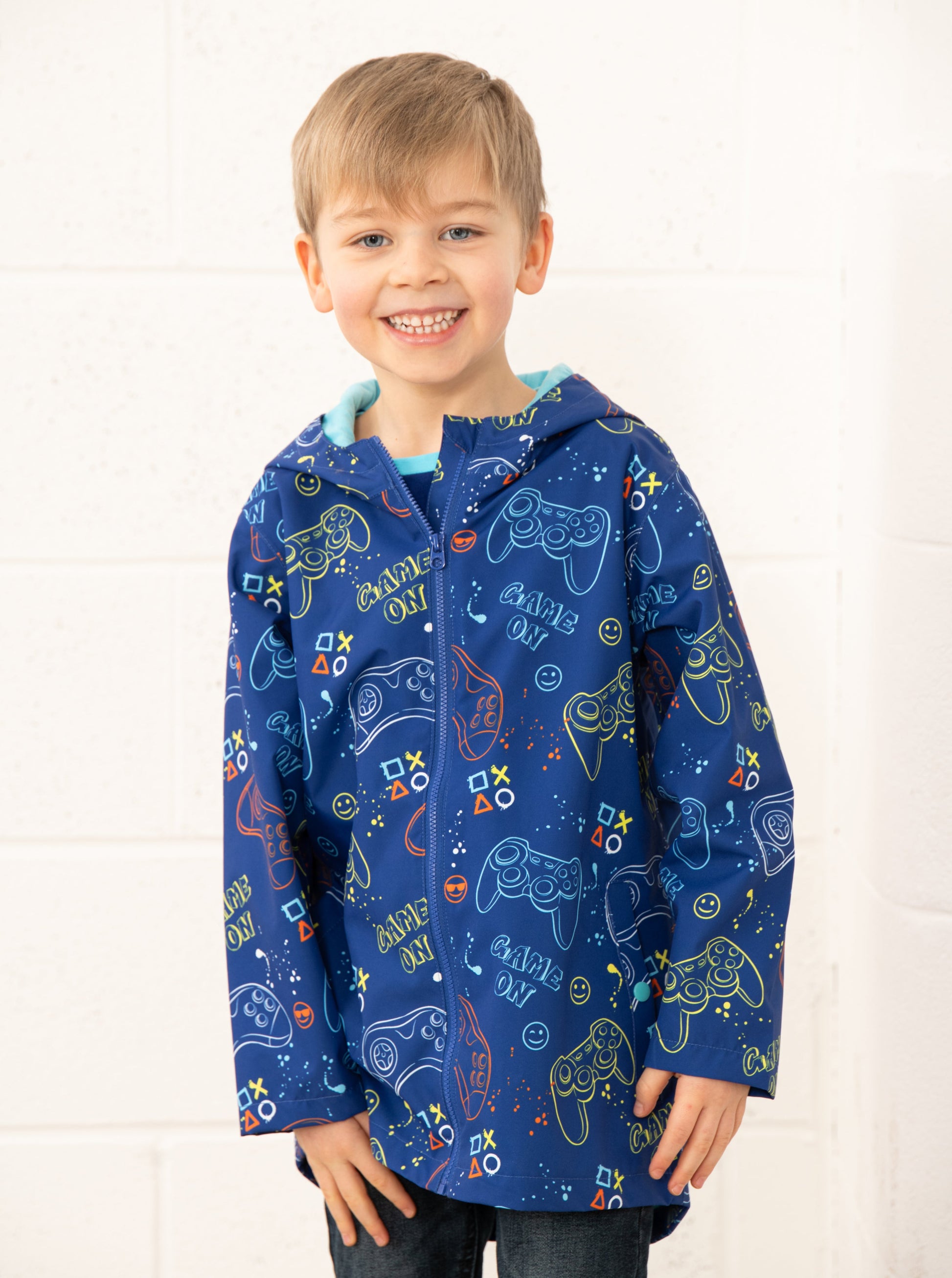 A child wearing a blue waterproof jacket with a gaming print, featuring an elasticated hood and popper pockets.