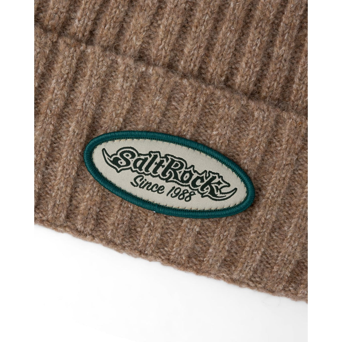 Close-up view of the turn back hem and logo patch of a Saltrock adults Legacy ribbed knit beanie in brown.