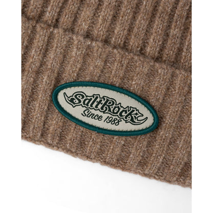 Close-up view of the turn back hem and logo patch of a Saltrock adults Legacy ribbed knit beanie in brown.