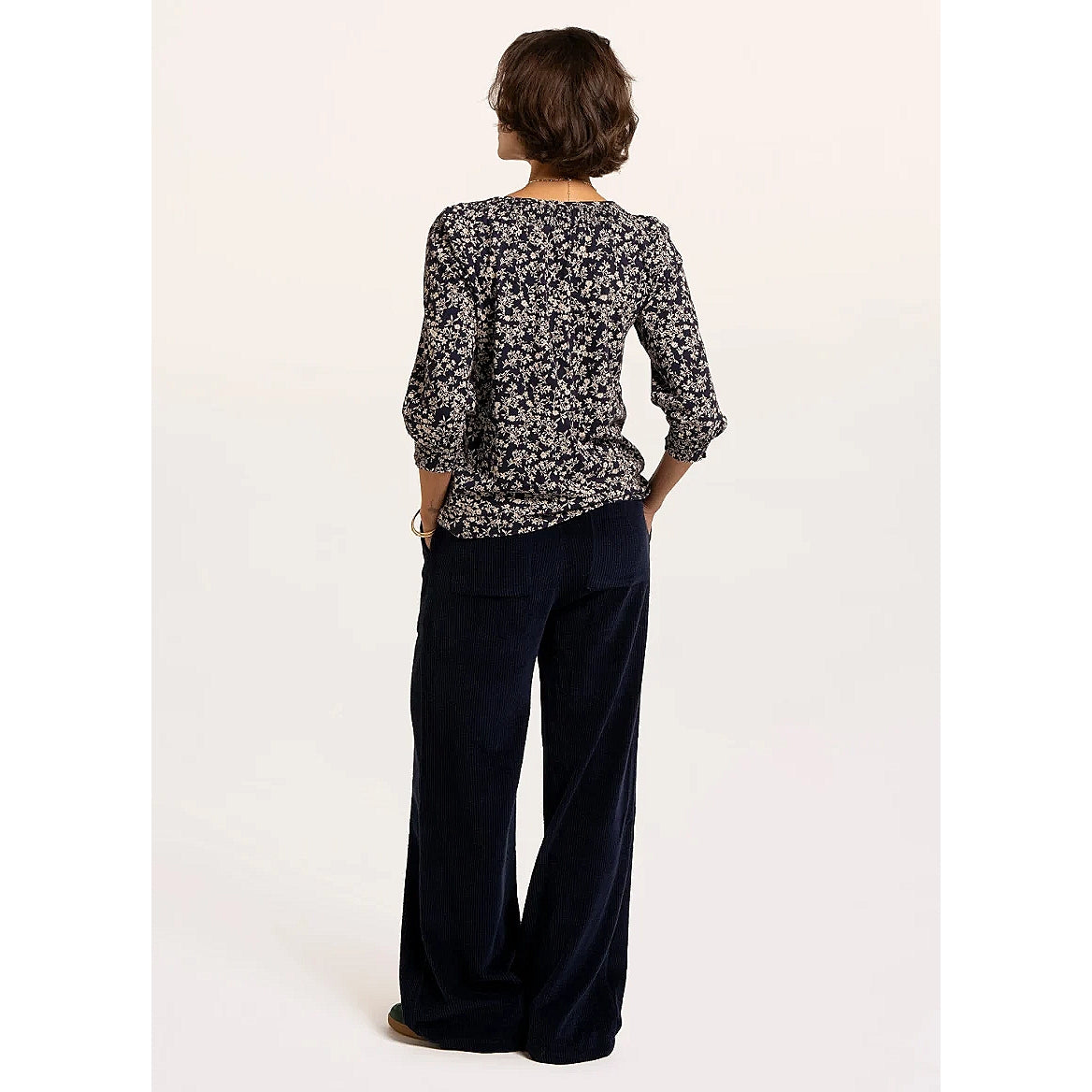 Back view of a woman wearing a Brakeburn Brielle 3/4 sleeve t-shirt in navy with a white floral pattern and elasticated cuffs and neckline trim.