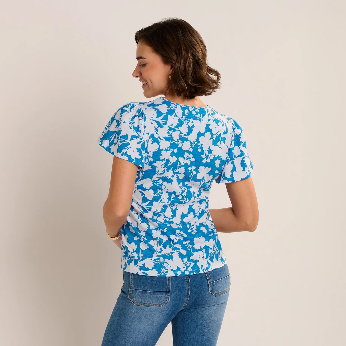 Back view of a woman wearing a Brakeburn short sleeve Ria blouse in blue with a white floral print.
