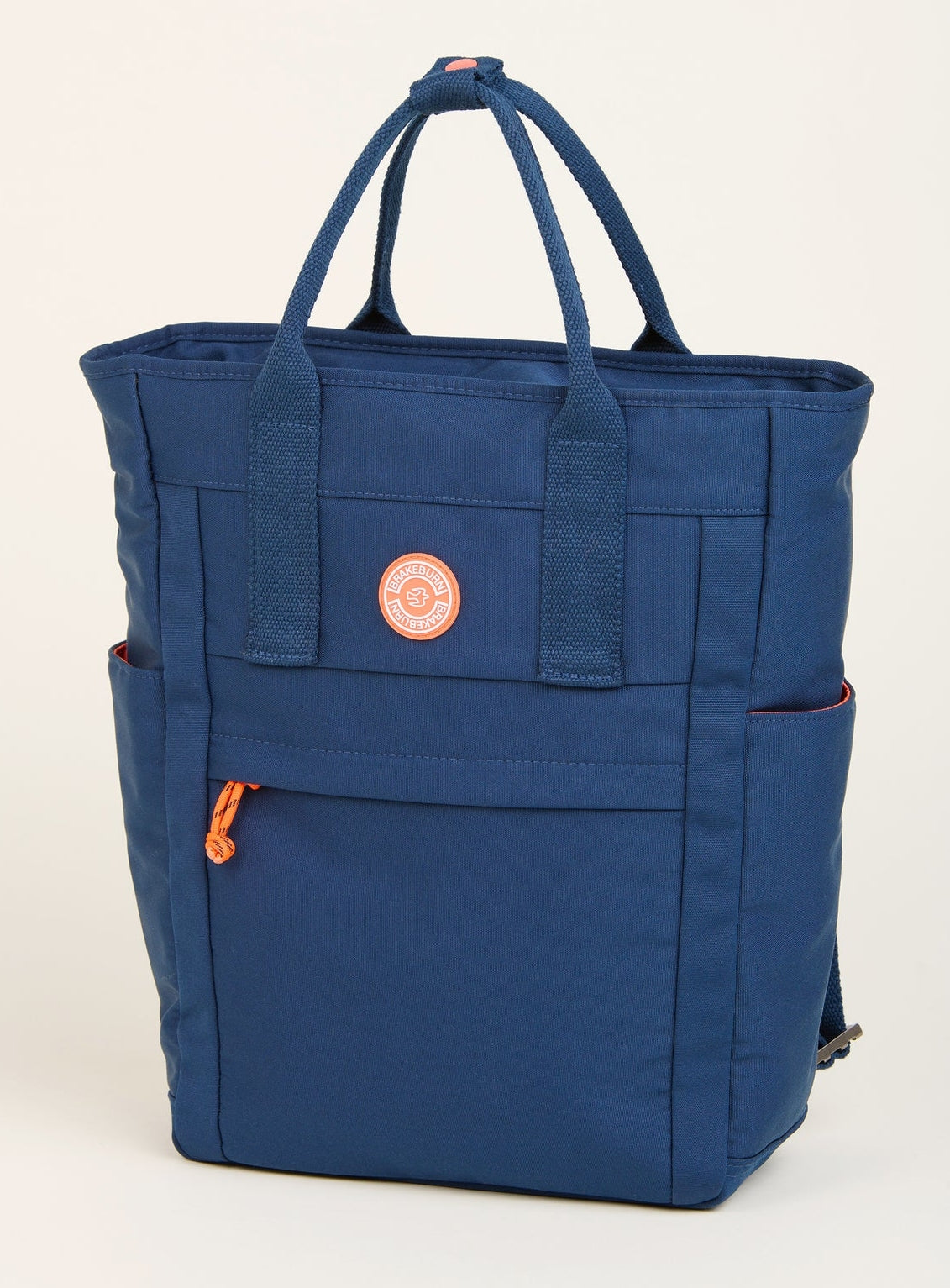 A navy blue Brakeburn Classic Tote Backpack with multiple compartments and orange straps, featuring a front zip pocket and side slip pockets.