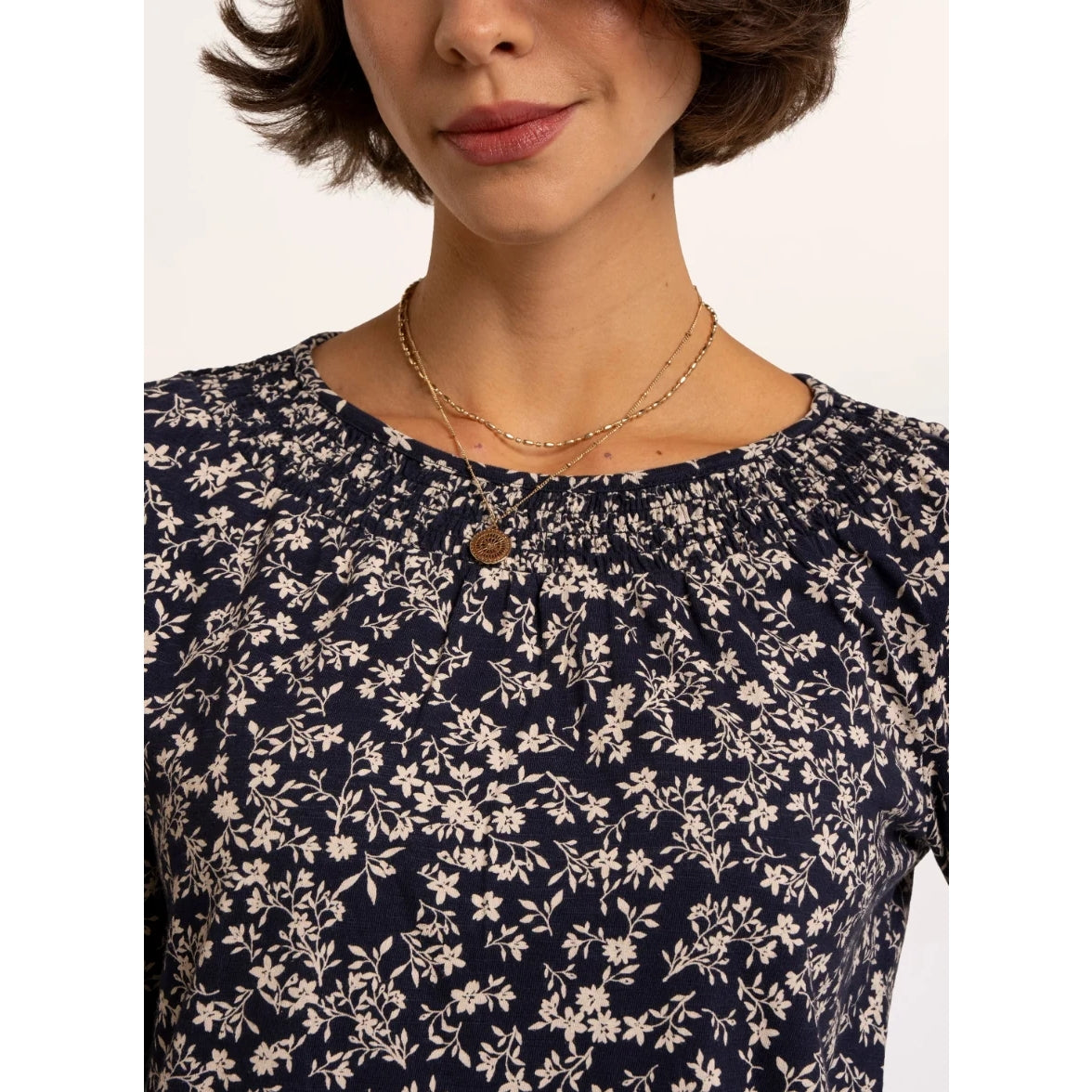 Close-up view of the neckline of a woman wearing a Brakeburn Brielle 3/4 sleeve t-shirt in navy with a white floral pattern and elasticated neckline trim.