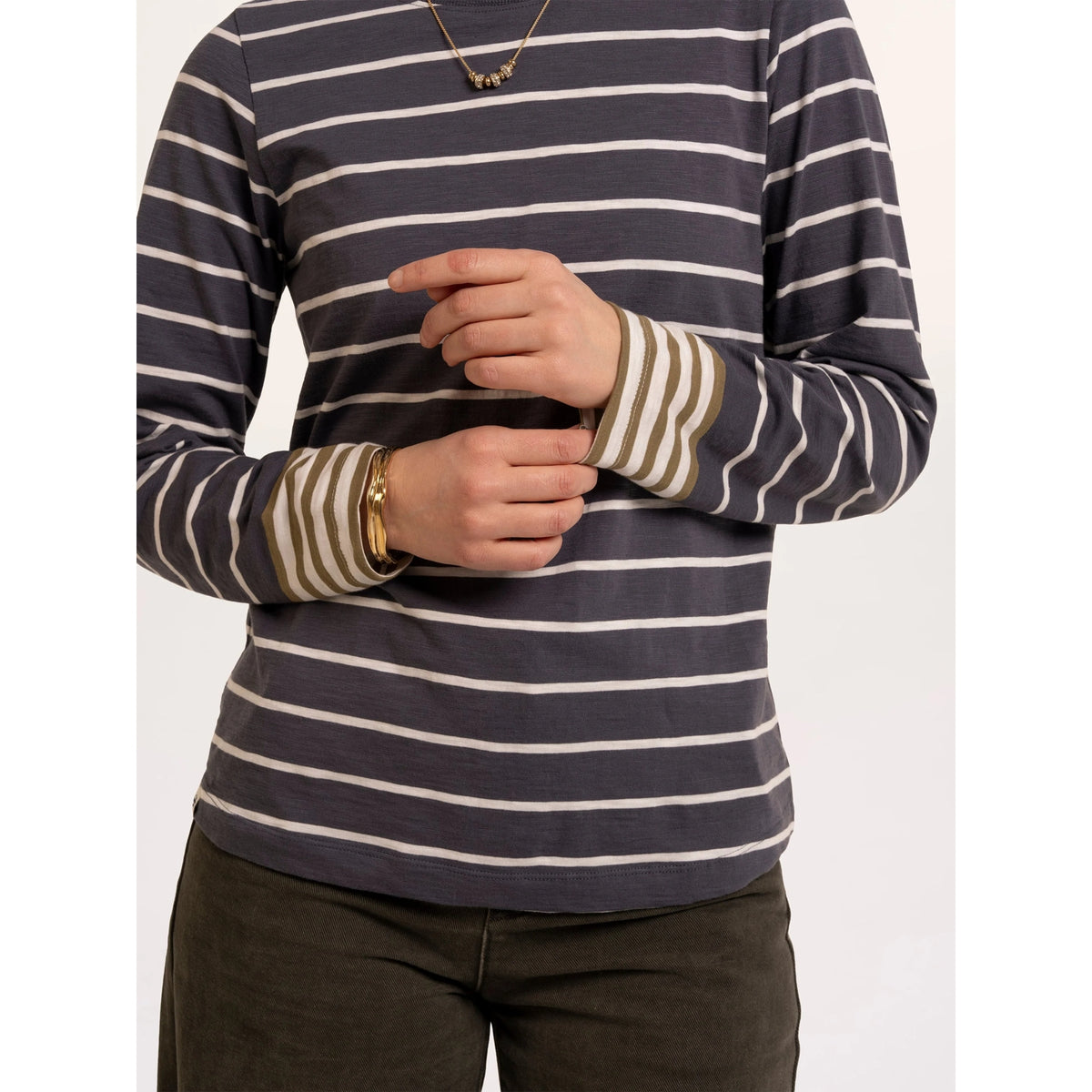 Close-up view of a woman wearing a Brakeburn long sleeve Exbury t-shirt in light navy with white stripes and contrasting mustard stripe cuffs.