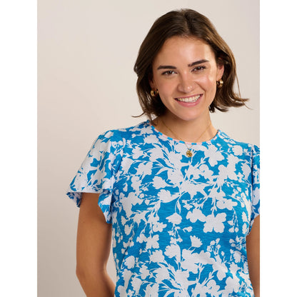 Close-up view of a woman wearing a Brakeburn short sleeve Ria blouse in blue with a white floral print.