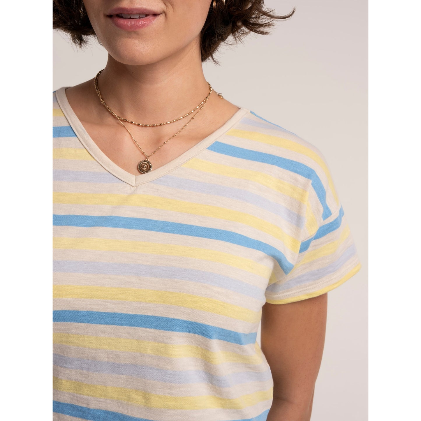 Close-up view of a woman wearing a Brakeburn short sleeve Seas t-shirt in a blue and yellow stripe pattern, with v-shape neckline.
