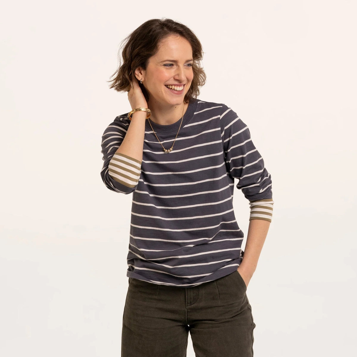 A woman wearing a Brakeburn long sleeve Exbury t-shirt in light navy with white stripes and contrasting mustard stripe cuffs.