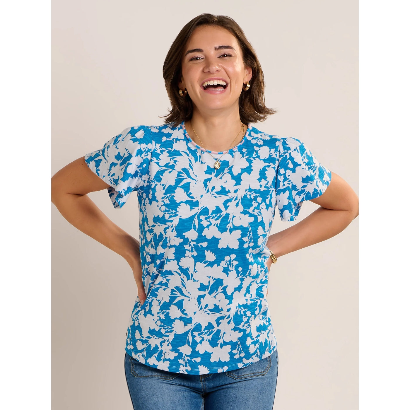 Front view of a woman wearing a Brakeburn short sleeve Ria blouse in blue with a white floral print and jeans.