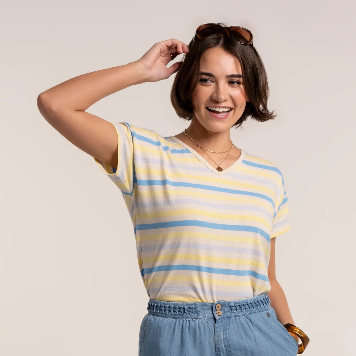 Woman wearing a Brakeburn short sleeve Seas t-shirt in a blue and yellow stripe pattern, with v-shape neckline with blue trousers.