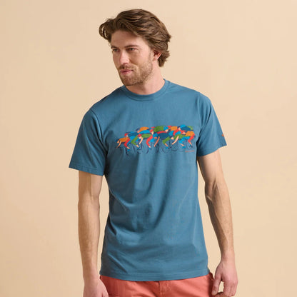Front view of a man wearing a blue Brakeburn short sleeve t-shirt with colourful Painted Peleton cycling graphic design on a beige background