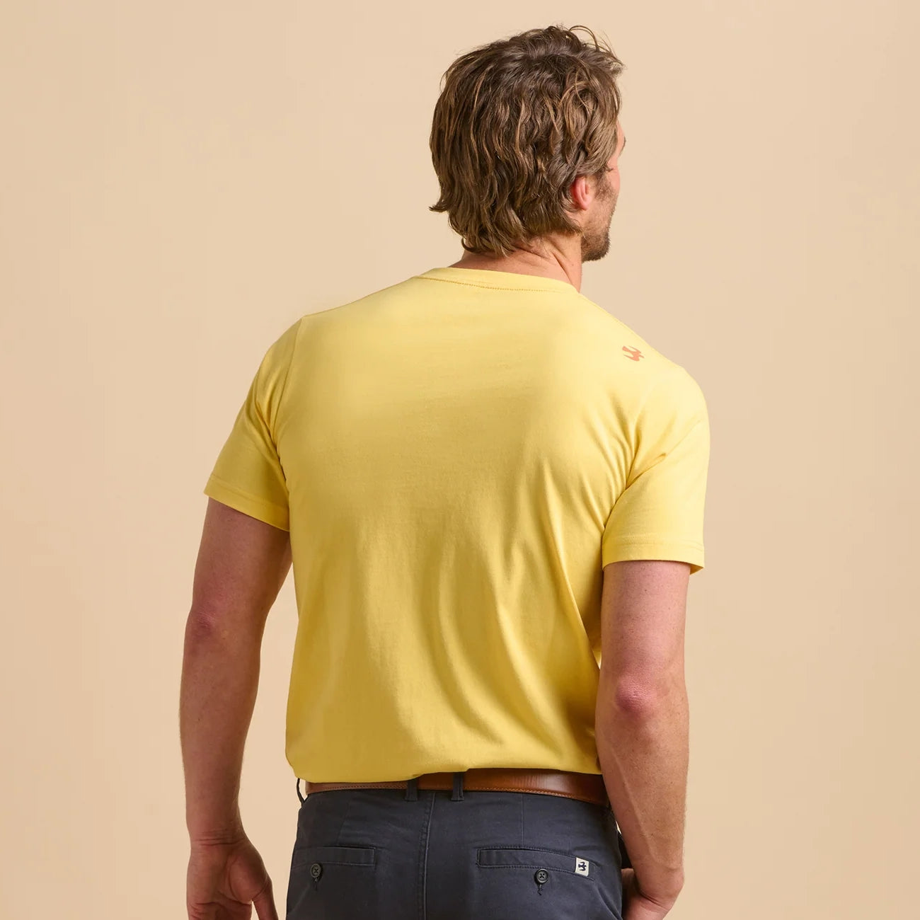 Back view of a man wearing a yellow Brakeburn t-shirt on a beige background