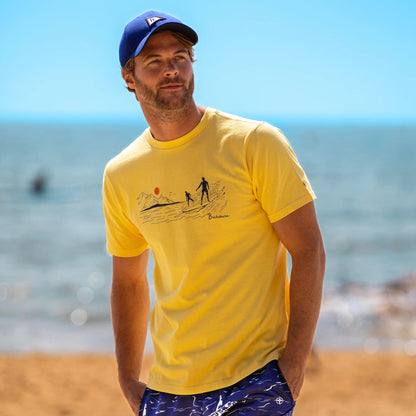Front view of a man wearing a Brakeburn yellow t-shirt with a South Coast Surf print design on a beach